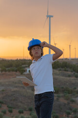 Engineer working on a wind farm at sunset. He watches the operating data of the windmills on his...