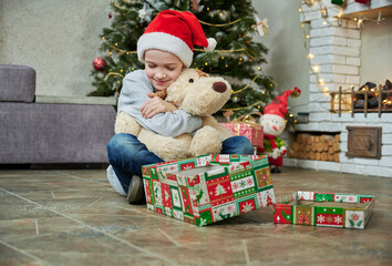 Cheerful kid girl opening Christmas gifts and hugs toy dog. Child with presents in room. Merry Christmas and Happy Holidays