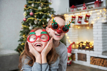 Laughing funny childen wearing Christmas costumes at home near christmas tree and fireplace....