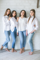 Pretty teenage girls models in trendy jeans and white shirts in the studio against the background of a white brick wall. Teenage fashion. beauty and fashion