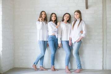 Pretty teenage girls models in trendy jeans and white shirts in the studio against the background of a white brick wall. Teenage fashion. beauty and fashion