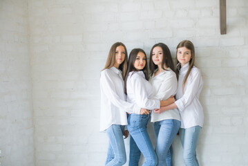 
Pretty teenage girls models in trendy jeans and white shirts in the studio against the background of a white brick wall. Teenage fashion. beauty and fashion