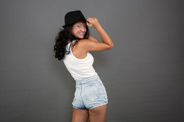 Young ethnic Asian woman posing in tank top, shorts and hat.