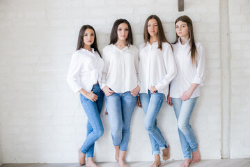 
Pretty teenage girls models in trendy jeans and white shirts in the studio against the background of a white brick wall. Teenage fashion. beauty and fashion