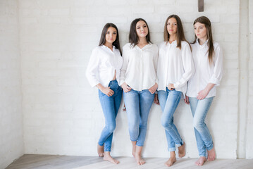 
Pretty teenage girls models in trendy jeans and white shirts in the studio against the background of a white brick wall. Teenage fashion. beauty and fashion
