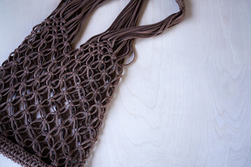 Brown string bag knitted in macrame technique from a knitted cord on a wooden background. Zero waste and plastic free concept. A place for your text, advertising. - obrazy, fototapety, plakaty