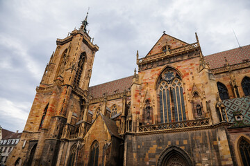 Colmar, Alsace, France, 4 July 2022: town capital of Alsatian wine, narrow picturesque street with medieval colorful houses, Roman Catholic Gothic St Martins Church with tower at summer day