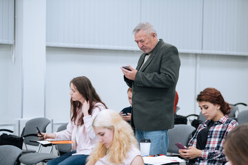 A teacher holds a smartphone in his hands during a lecture for students at a university. Chatting anywhere at any time