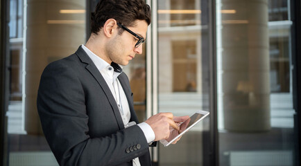 A male manager uses an app on a tablet, goes to work in a new office in a suit