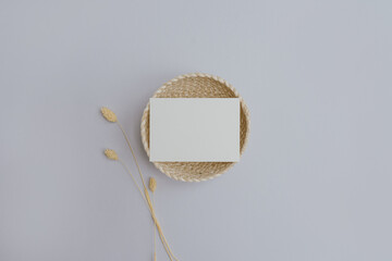 Flatlay blank paper sheet, rattan plate, rabbit tail grass stem on pastel purple background. Home office desk workspace. Business, work template. Flat lay, top view