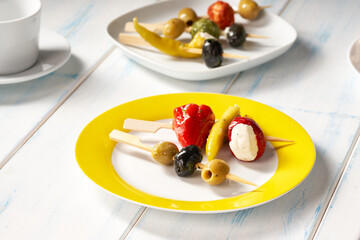 Finger food sticks with olives and stuffed pepperoni on yellow plate.