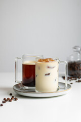 Two cups of coffee. Hot coffee in the background, coffee ice with milk in the foreground (a coffee drink made from ice cubes of coffee). Behind the coffee cups is a jar of coffee beans.