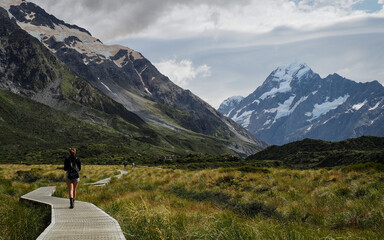 Mount Cook, Aoraki, New Zealand.

Young woman walking along a wooden path in the Mount Cook National Park. Beautiful views of marshland and snow topped mountains.