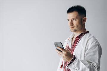 Guy in Ukrainian vyshyvanka stands holding phone and chatting.