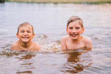 Emotional portrait of two cute happy wet school age boys inside the lake. Preteen boy swimming in lake. Summer cump, happy childhood, active lifestyle concept.