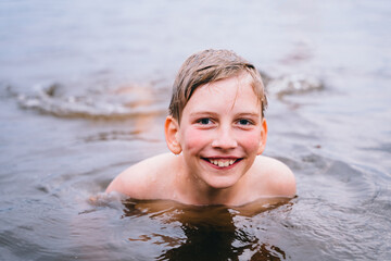 Close up portrait of cute happy wet school age boy inside the lake. Preteen boy swimming in lake at forest.