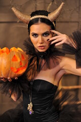 Close-up of a beautiful brunette woman with horns and festive makeup with black manicure and black clothes. Halloween makeup.