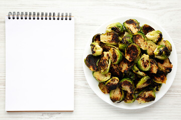 Homemade Roasted Brussel Sprouts on a Plate, blank notepad, top view. Flat lay, overhead, from above.