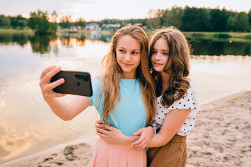 Vacation, relax, active lifestyle concept. Two teenager girls friends in eyeglasses having fun, laughing, taking selfie by smartphone at nature by the lake.