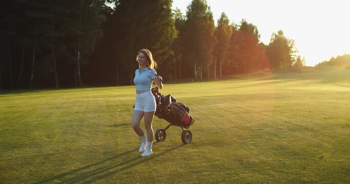 Cheerful woman Pulling Bag with Golf Clubs for Playing on a summer evening. High quality 4k footage