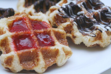 Waffles topped with chocolate and strawberries served in a white plate.