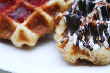 Waffles topped with chocolate and strawberries served in a white plate.