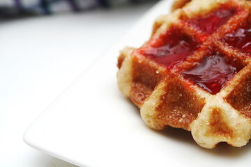 Waffles topped with chocolate and strawberries served in a white plate.