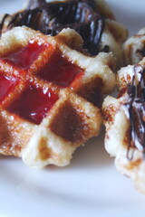 Waffles topped with chocolate and strawberries served in a white plate.