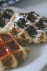 Waffles topped with chocolate and strawberries served in a white plate.