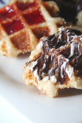 Waffles topped with chocolate and strawberries served in a white plate.