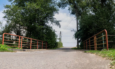 Krajobraz wiejski w porze letniej, most i drzewa z żabiej perspektywy, asfaltowy most ogrodzony dwiema poręczami