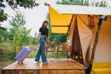 Fototapeta na wymiar Woman traveler with luggage moving towards bedroom of cozy glamping house. Luxury camping tent for outdoor summer holiday and vacation. Lifestyle concept