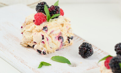 Baked meringue roll with cream and fresh fruits on a white wooden board, delicious dessert