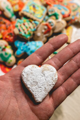 Hand holding a delicious handmade heart cookie and plate with more holiday cookies on a tea time table