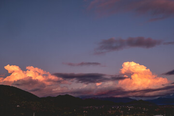 Amazing clouds with orange sunlight over purple sunset sky and mountains silhouette with little village