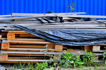 Old wooden pallets are stored near the fence on a summer day