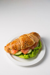 Croissant with salmon and cucumber on a white plate