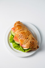 Croissant with salmon and cucumber on a white