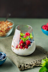 Tasty homemade granola with yogurt and berries on a green background. Granola and healthy breakfast ingredients with green napkin