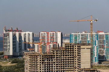 Yellow construction tower crane against the background of multi-apartment residential buildings under construction