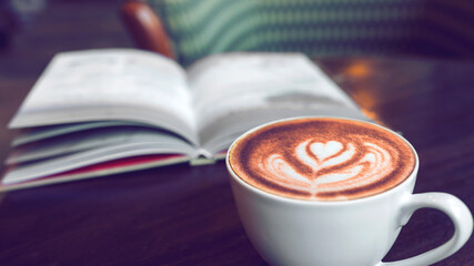 Late art coffee cup on blur book background at coffee shop in the morning, classic retro warm tone	