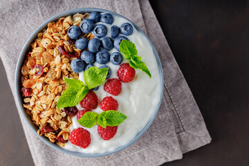 Healthy breakfast with homemade granola, yogurt, blueberry and raspberry. Greek yogurt with granola, berries and mint in a gray bowl. Top view. Copy space