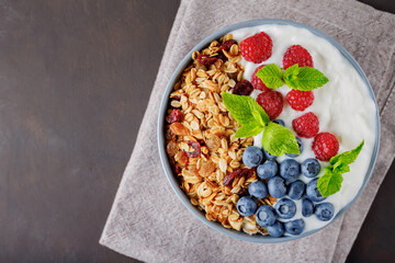 Healthy breakfast with homemade granola, yogurt, blueberry and raspberry. Greek yogurt with granola, berries and mint in a gray bowl. Top view. Copy space