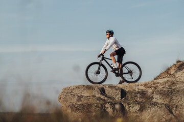 Equipped Professional Male Cyclist Standing with Mountain Bike on Edge of the Rock, Sky on the...
