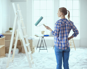 Beautiful young woman doing wall painting, standing near ladder