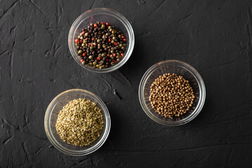 Various spices in three containers. Pepper, coriander, oregano. Dark background. Close-up.