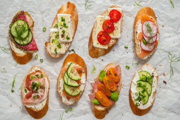 Variety of small sandwiches with cream cheese, vegetables and salami.