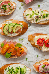 Variety of small sandwiches with cream cheese, vegetables and salami.