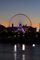Long exposure of Montreal Grand Ferris Wheel in Old Port with motion blurat twilight blue hour. Reflections of sun rays on Saint Laurent river with a background of cloudy blue sky