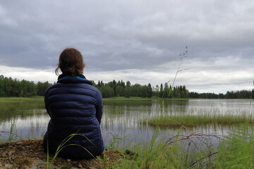 Girl sitting at a lake. Watching the view. One cloudy Swedish summer day. J&auml;mtland, Sweden, Europe.